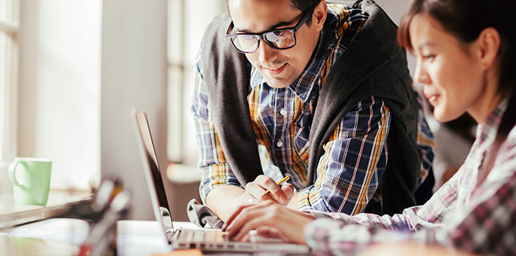 a woman works on a laptop while a man looks on