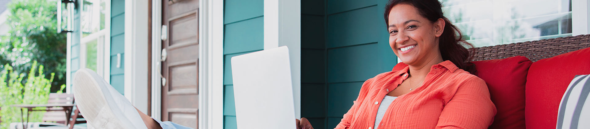  Woman sits on a porch loveseat working on a laptop