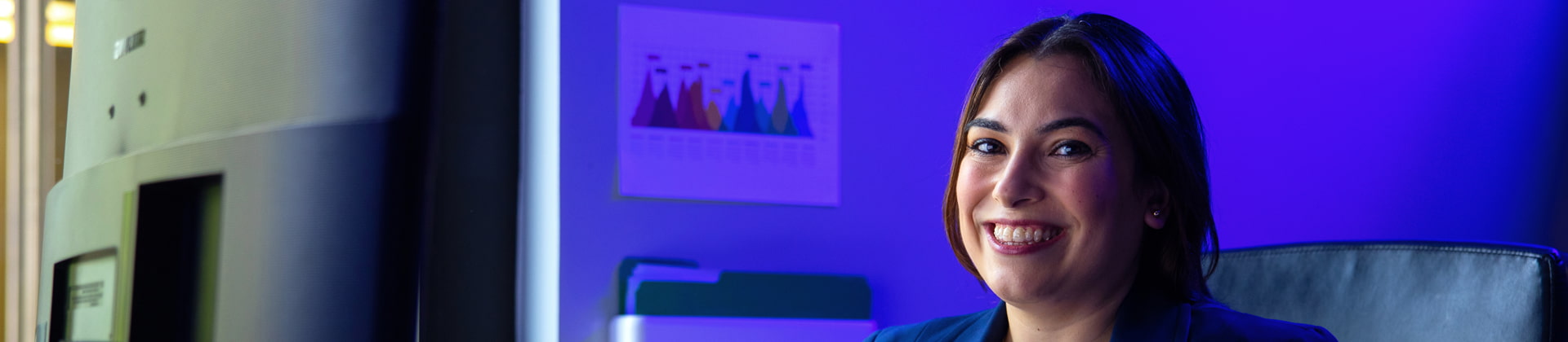 Nadia L. sits in an office with a purple background