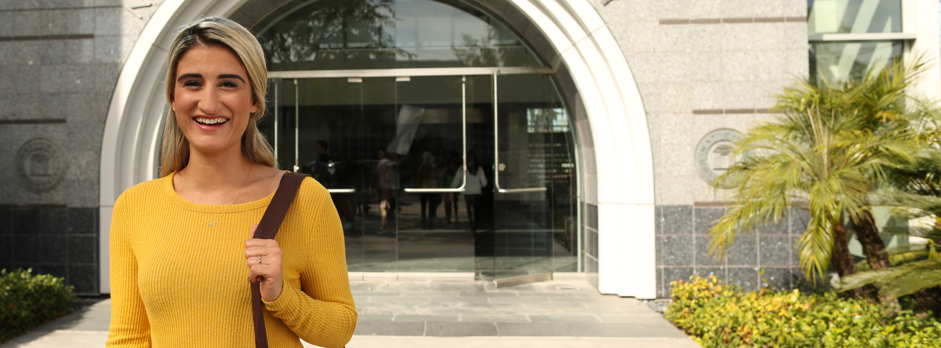 woman smiling with shoulder bag in front of national university building