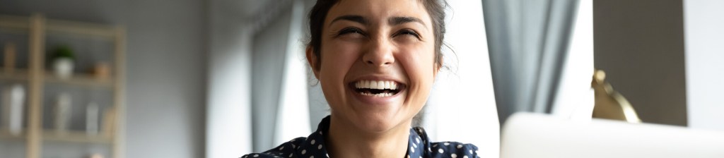 woman at home smiling as she looks above her laptop