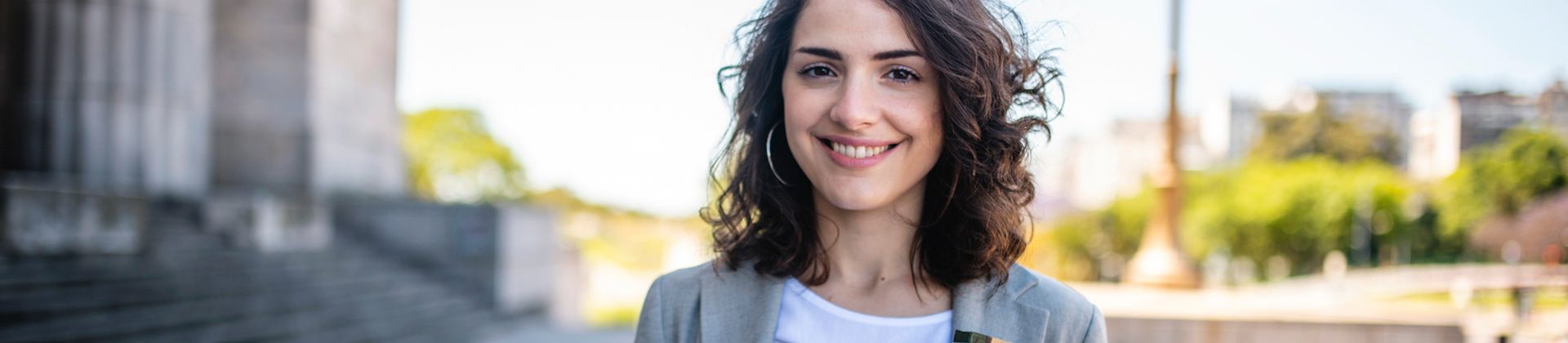 Woman with curly hair wearing a blazer stands outside with greenery in the background. Minor in Pre-Law Studies Program Page