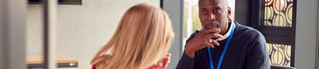 Black professional teacher looking concerningly at student whose back is turned towards camera but appears to be crying