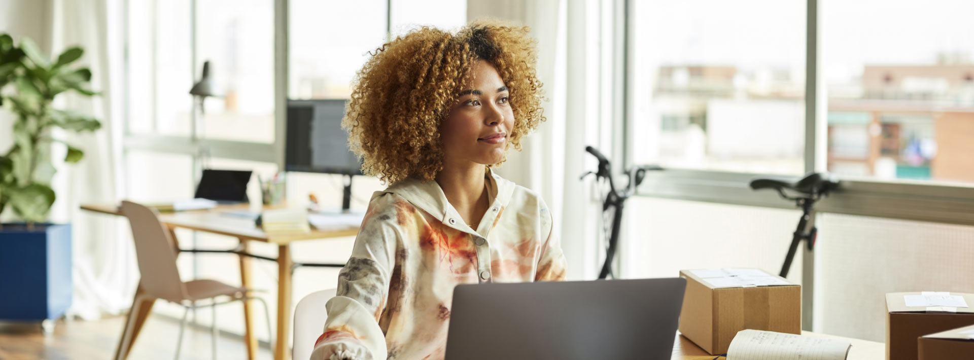 A woman with blonde curly hair sits in front of a laptop in office