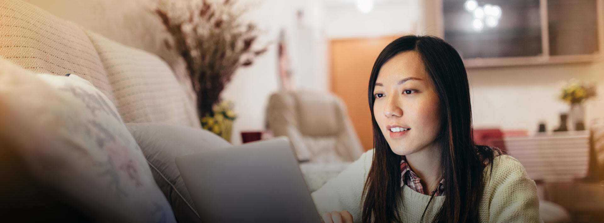 Woman with straight brown hair and wearing a sweater looks at a laptop screen in her living room.