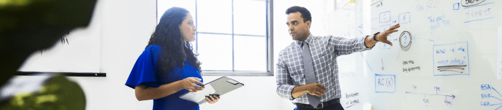 man looking at woman as he points to whiteboard