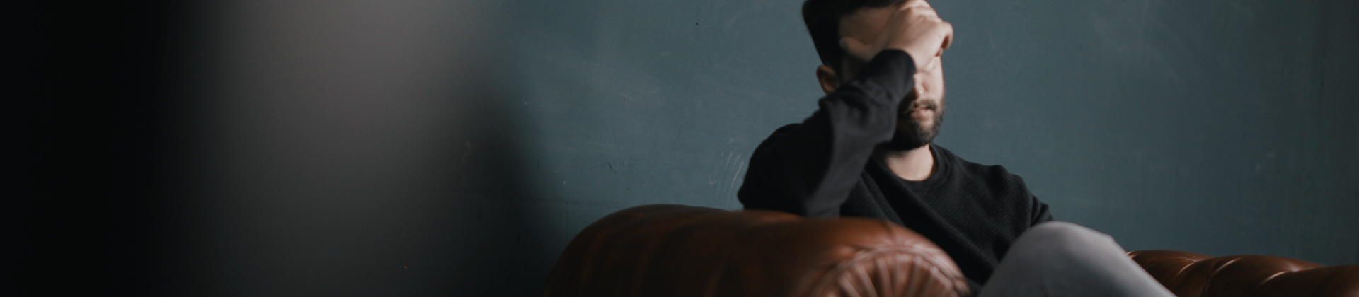 man sitting on sofa with hand on head looking sad