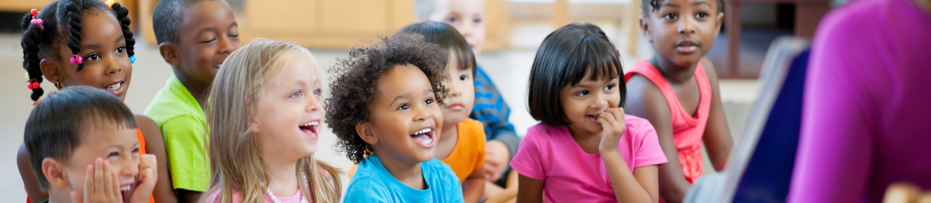 a group of kindergarten age students sit together looking at someone out of frame