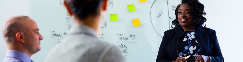 men and women talk in front of a white board filled with facts and figures 