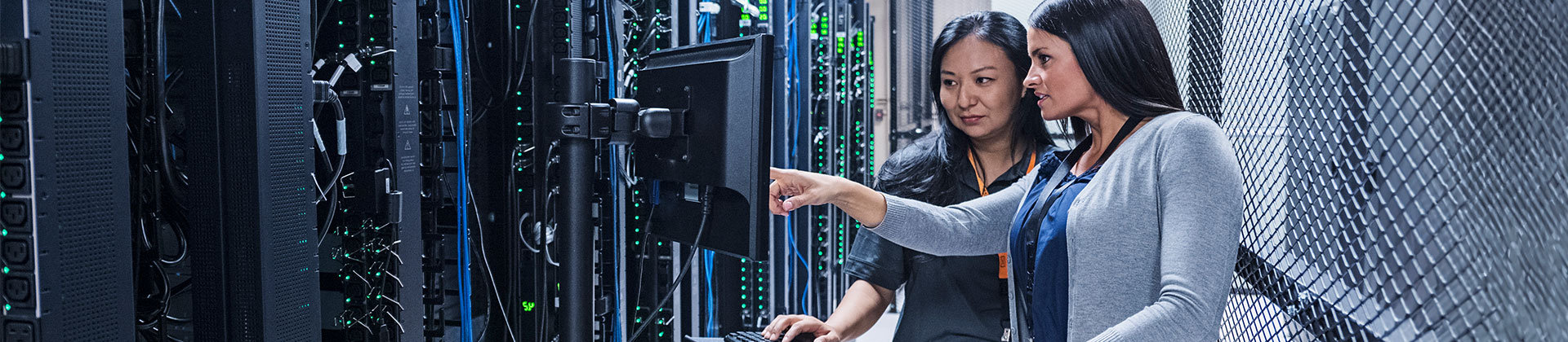 two women look at a computer screen in a server room