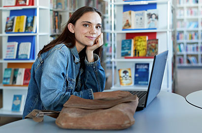 Woman sitting at desk in a library working on their laptop