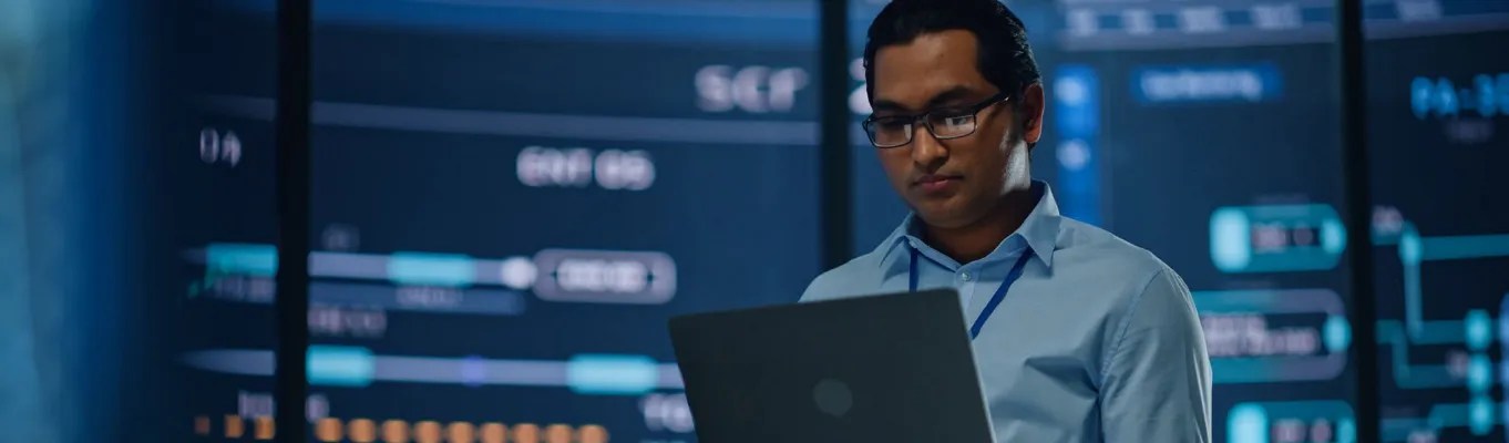 man working on laptop in dark room with servers around them